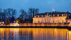 Das weihnachtlich erleuchtete Schloss Benrath mit Blick über den See.