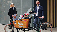 Personen stehen neben einem Lastenfahrrad, zwei Kinder sitzen drin