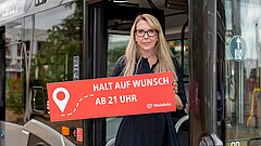 Frau steht vor einem Bus und hält ein Schild hoch
